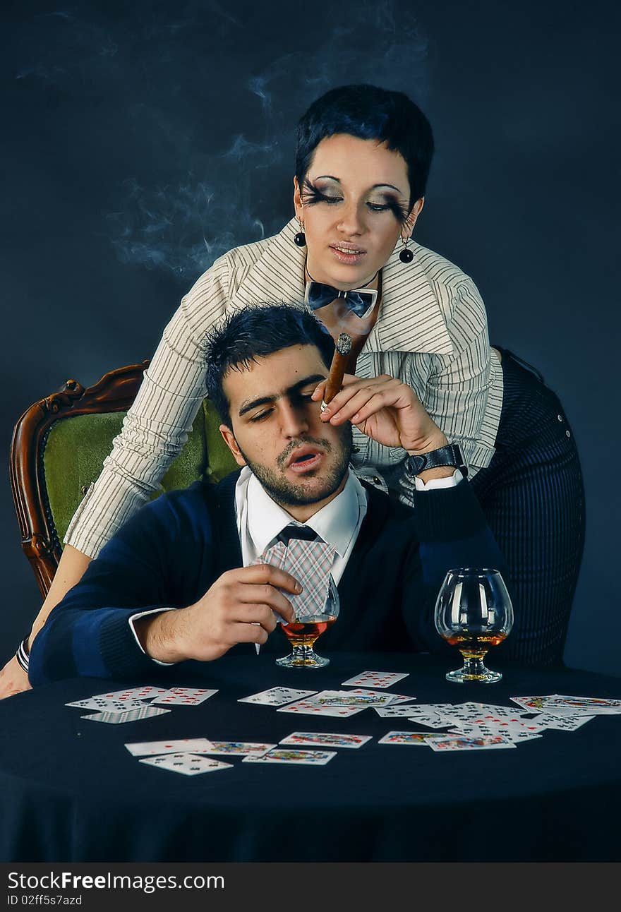 There is cool couple. He smokes cigar and holds cards. There is cool couple. He smokes cigar and holds cards.