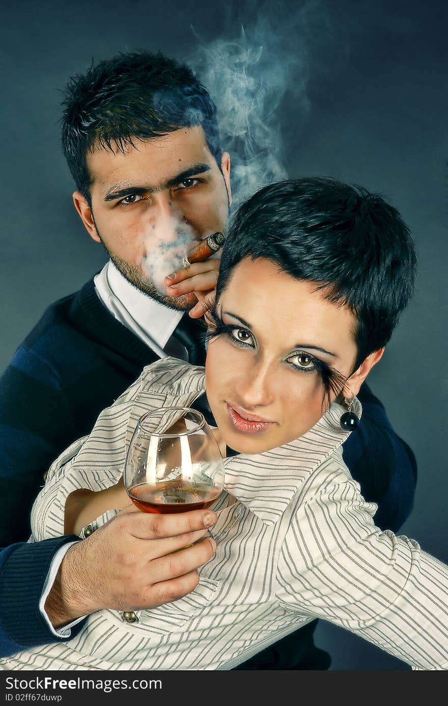 There is cool couple. He smokes cigar and hold glass with cognac. There is cool couple. He smokes cigar and hold glass with cognac.