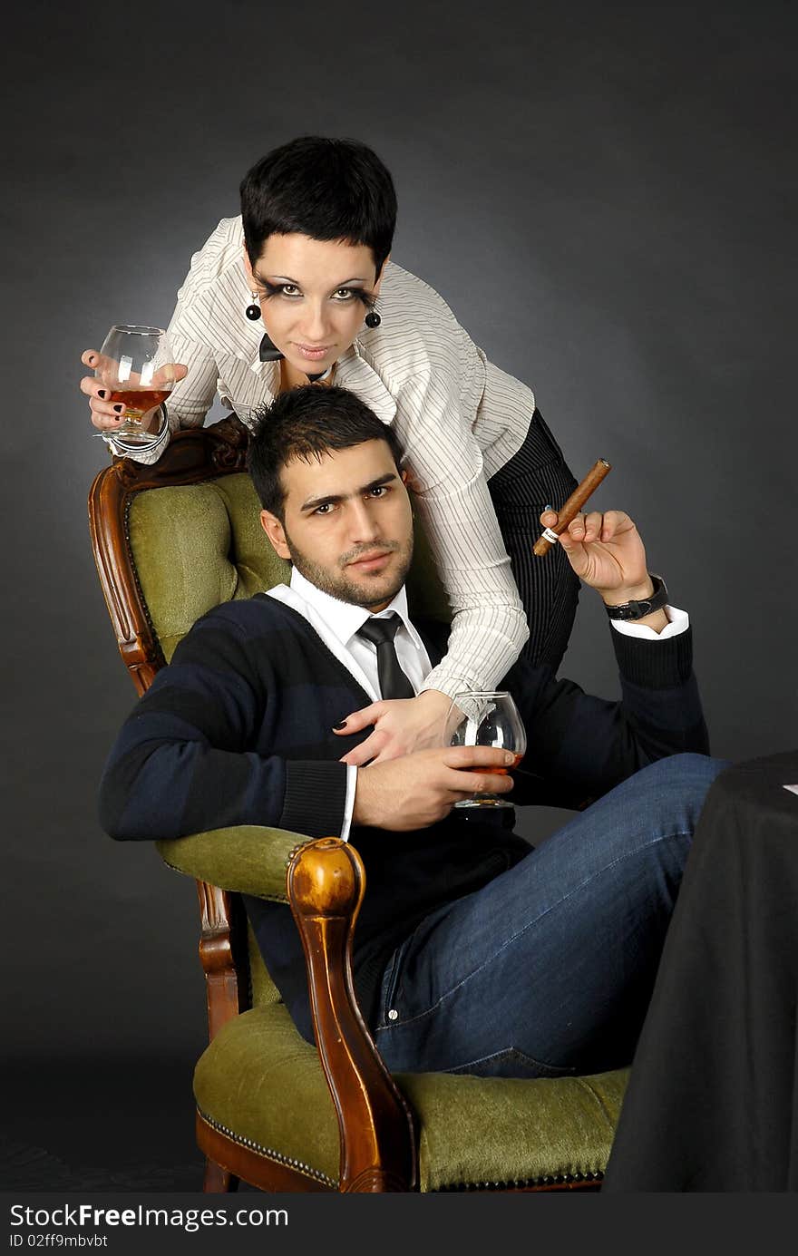 There is cool couple. He smokes cigar and hold glass with cognac. There is cool couple. He smokes cigar and hold glass with cognac.