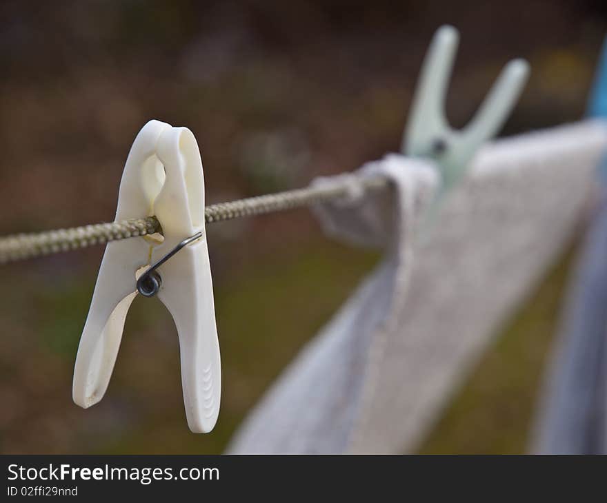 White clothespin on clothes line with laundry in background.