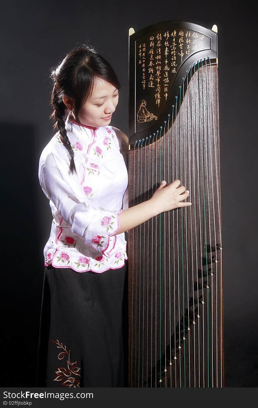 Chinese zither performer in traditional dress with her zither on dark. Chinese character on zither is Chinese Tang poetry,also a famous Tang Dynasty poet's calligraphy. It praised the unique charm of the zither. Chinese zither performer in traditional dress with her zither on dark. Chinese character on zither is Chinese Tang poetry,also a famous Tang Dynasty poet's calligraphy. It praised the unique charm of the zither.