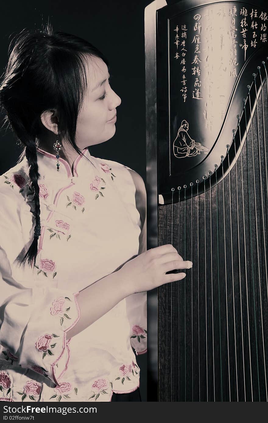 Chinese zither performer in traditional dress with her zither on dark. Chinese character on zither is Chinese Tang poetry,also a famous Tang Dynasty poet's calligraphy. It praised the unique charm of the zither. Chinese zither performer in traditional dress with her zither on dark. Chinese character on zither is Chinese Tang poetry,also a famous Tang Dynasty poet's calligraphy. It praised the unique charm of the zither.