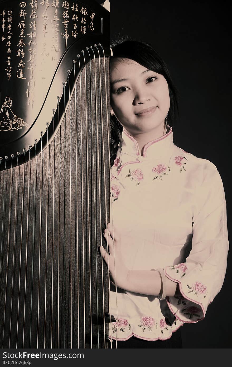 Chinese zither performer in traditional dress with her zither on dark. Chinese character on zither is Chinese Tang poetry,also a famous Tang Dynasty poet's calligraphy. It praised the unique charm of the zither.