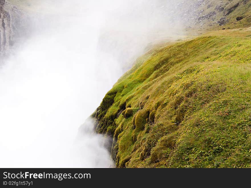 Detail of the Gullfoss waterfall in Iceland, wild water mist with mountains of green grass and moss