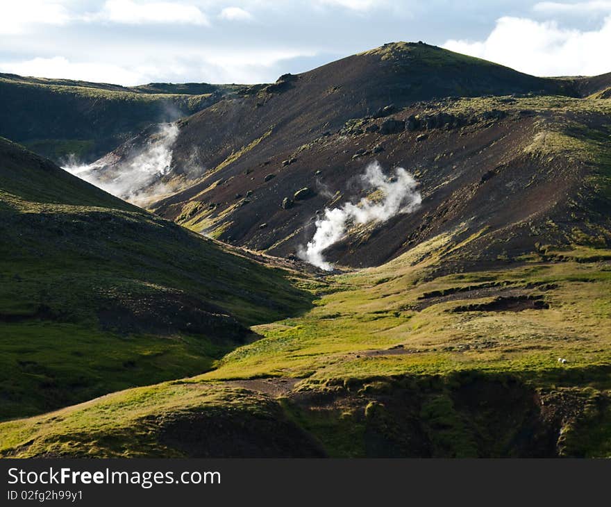 Steaming river, black lava mountains and sheep in