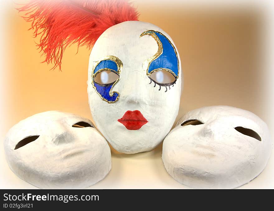 Hand made papier mache carnival mask decorated with blues and gold and a red plume shown with two unfinished masks in a still life arrangement. Hand made papier mache carnival mask decorated with blues and gold and a red plume shown with two unfinished masks in a still life arrangement