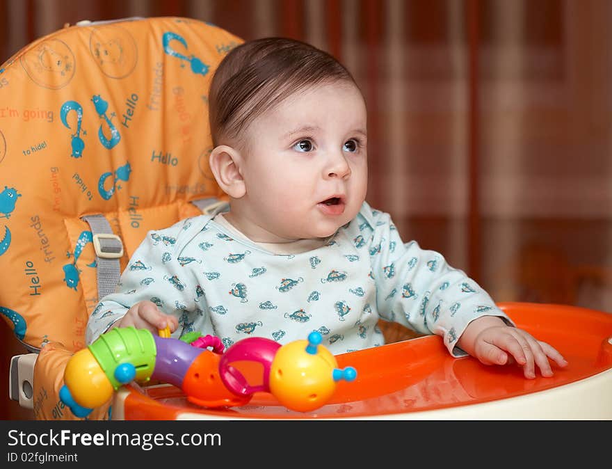 Half-year-old kid sitting on a chair for feeding and playing. His playful mood, but he was surprised. Half-year-old kid sitting on a chair for feeding and playing. His playful mood, but he was surprised