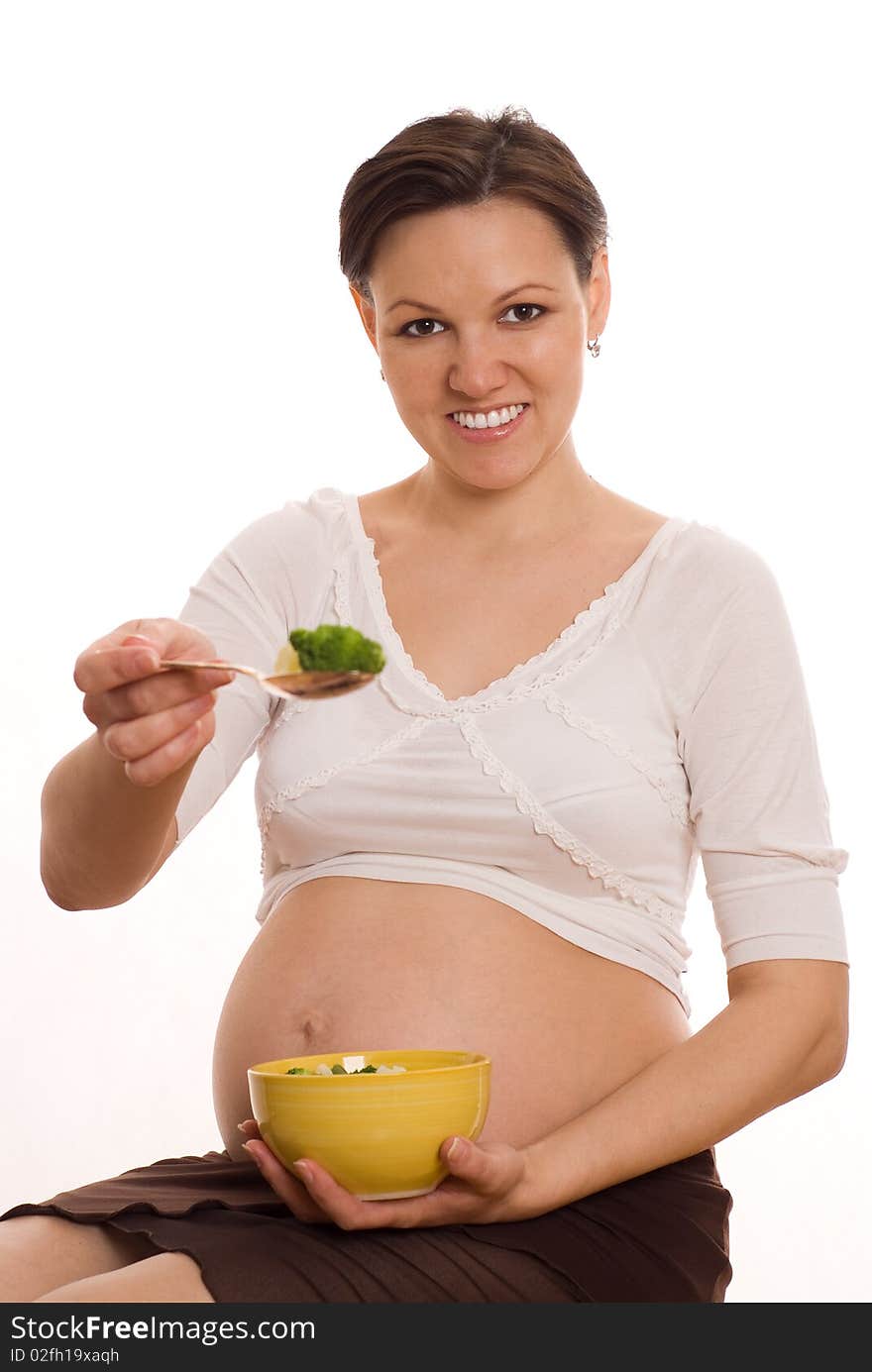 Beautiful pregnant woman eats vegetables on white. Beautiful pregnant woman eats vegetables on white