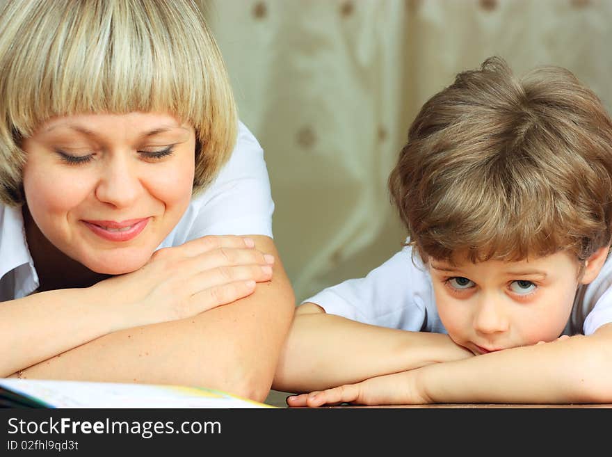 Woman and little boy lying down on the floor and reading a book. Woman and little boy lying down on the floor and reading a book