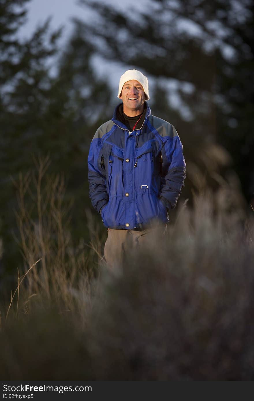 Portrait of a smiling man standing in a clearing in the wilderness. He is wearing a coat and hat. Vertical format. Portrait of a smiling man standing in a clearing in the wilderness. He is wearing a coat and hat. Vertical format.