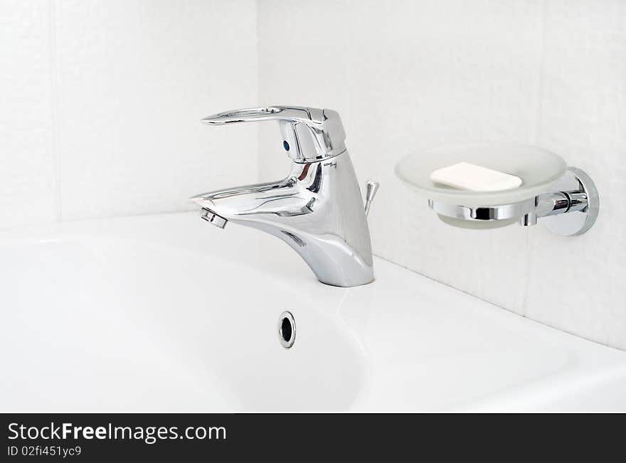 One chrome faucet in washbowl in bath room o white pile with soap holder. One chrome faucet in washbowl in bath room o white pile with soap holder