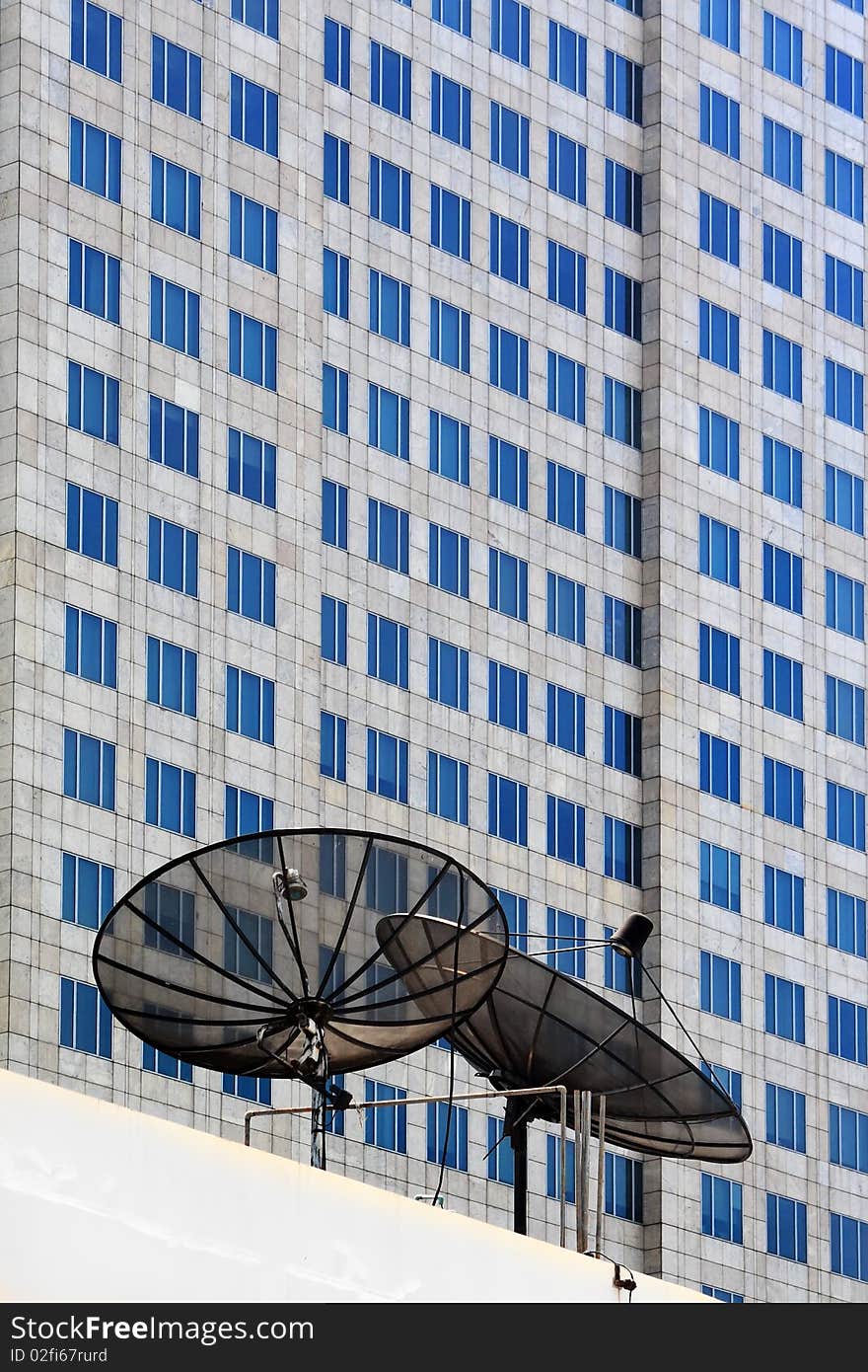 Dish of satellite on building and background is blue glass windows