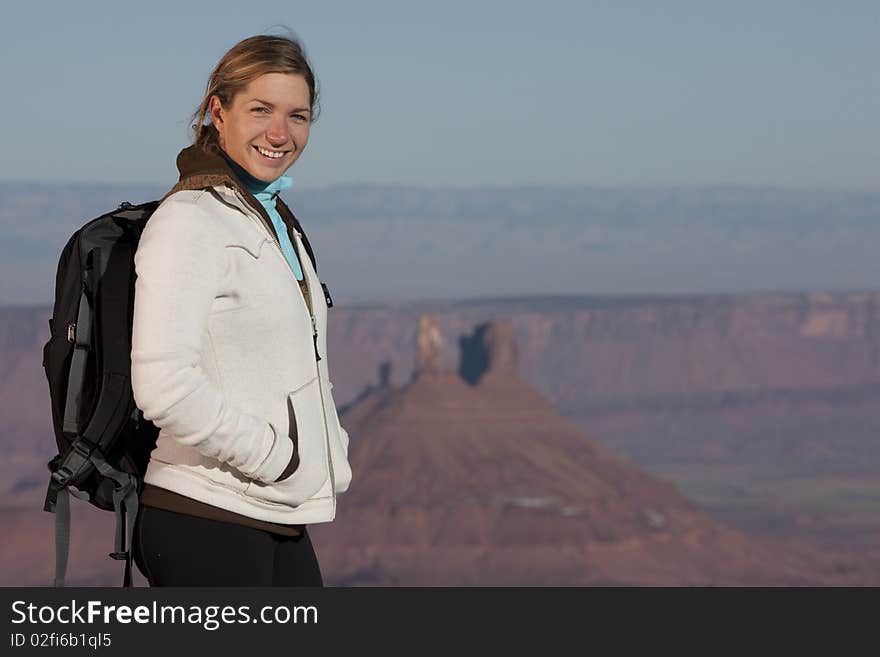 A young female hiker wearing a black backpack smiles at the camera. In the background is a desert landscape. Horizontal shot. A young female hiker wearing a black backpack smiles at the camera. In the background is a desert landscape. Horizontal shot.