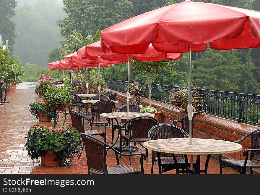 Patio tables with red umbrellas during the rain