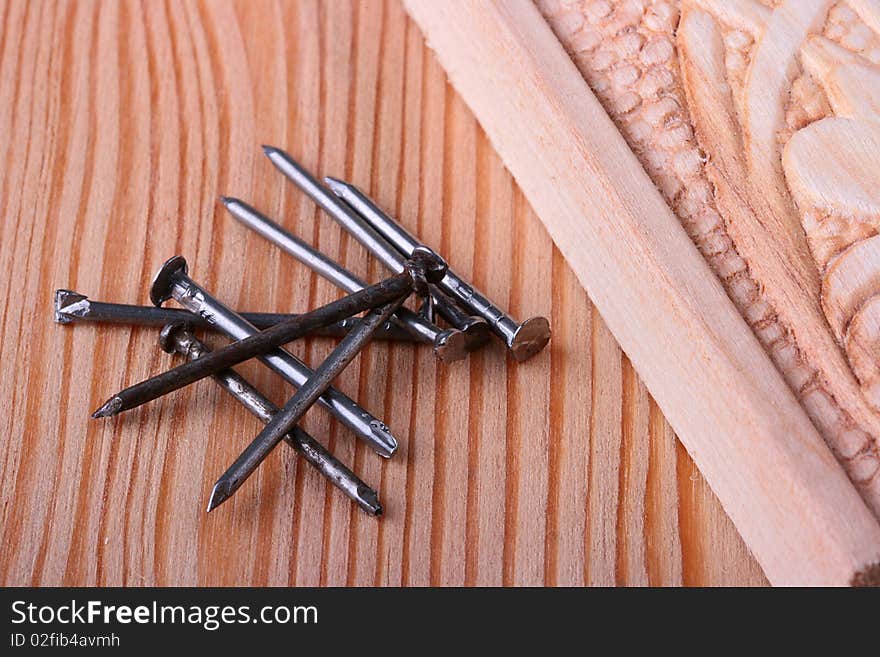 Nails for building and repair work, nearby a wooden board with a decorative carving.