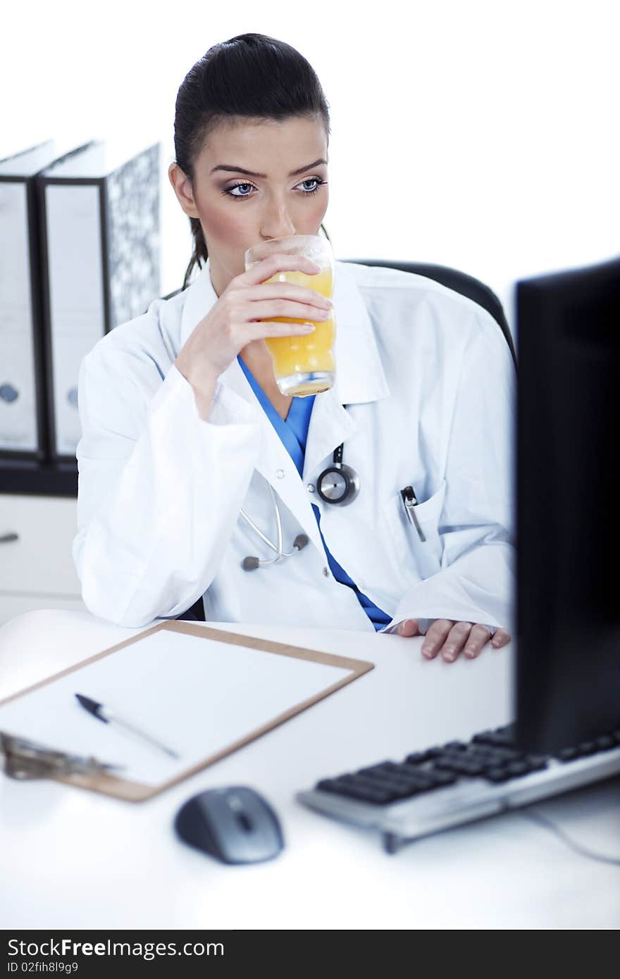 Doctor drinking a glass of juice at her workplace over white background