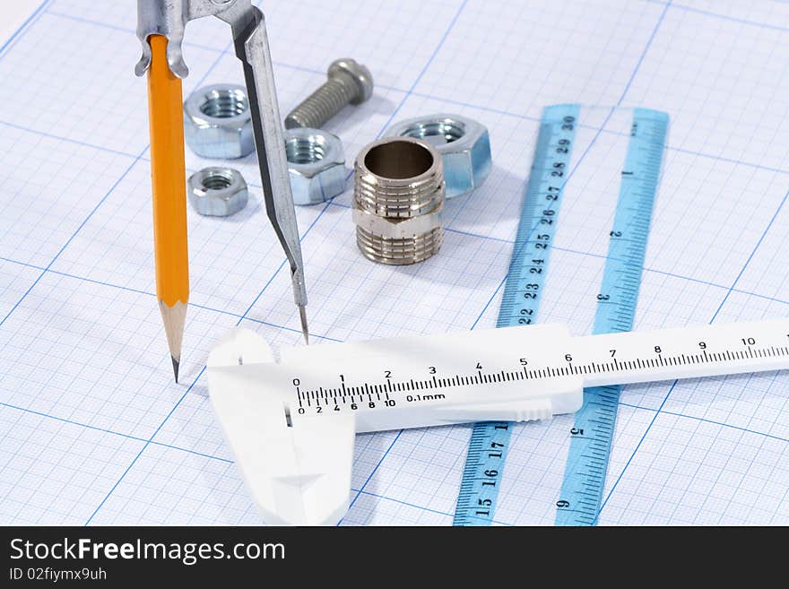 Divider, pencil, caliper, ruler and few screw nuts on graph paper background. Divider, pencil, caliper, ruler and few screw nuts on graph paper background