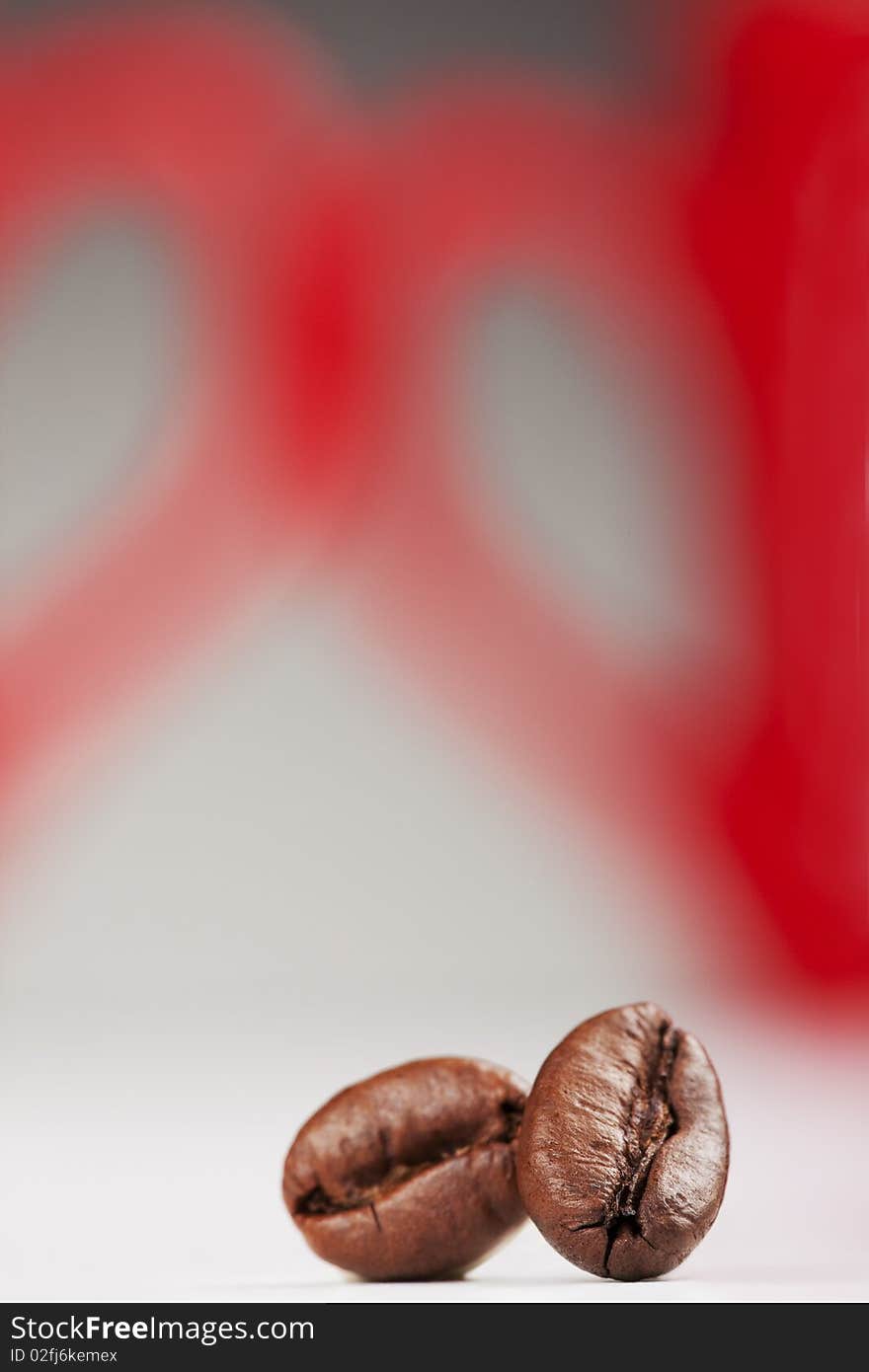 Two coffee beans against red cup`s handles, representing the two halves of the heart. Two coffee beans against red cup`s handles, representing the two halves of the heart