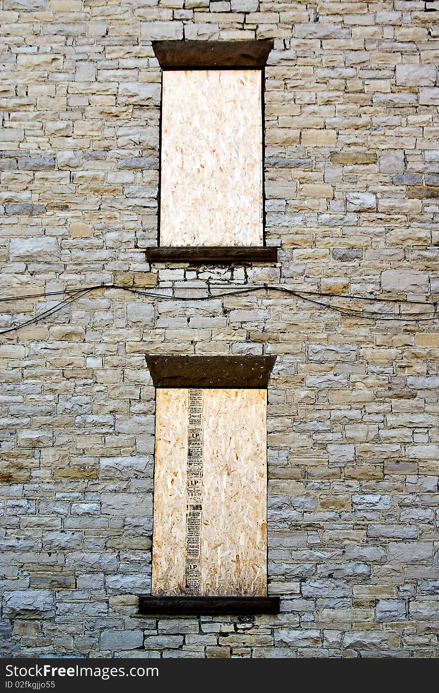 Two boarded-up windows on a stone wall texture. Two boarded-up windows on a stone wall texture.