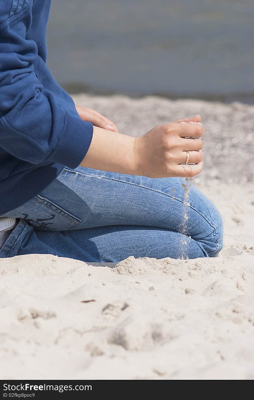 Woman in blue jeans sitting on the beach with the sand pouring out from her hand with the golden ring. Woman in blue jeans sitting on the beach with the sand pouring out from her hand with the golden ring