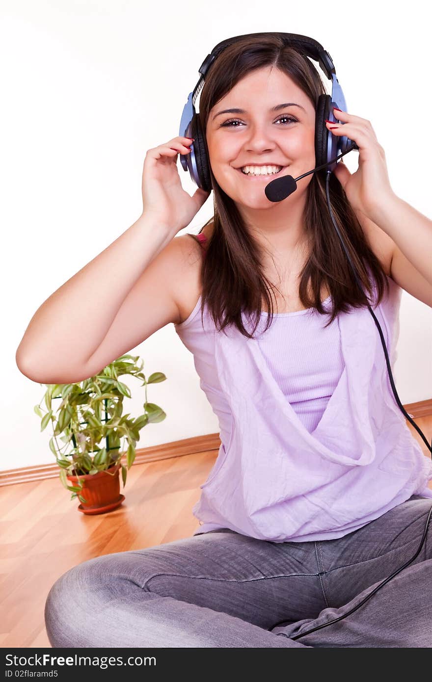 Smiling young brunette girl sitting on the floor with earphones on her head. Smiling young brunette girl sitting on the floor with earphones on her head