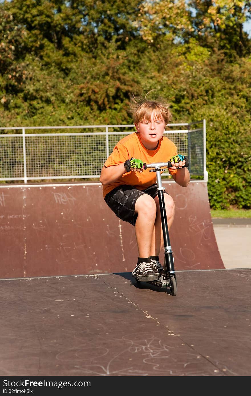 Child, boy is jumping with a scooter over a fun box in the skate parc and enjoying it. Child, boy is jumping with a scooter over a fun box in the skate parc and enjoying it