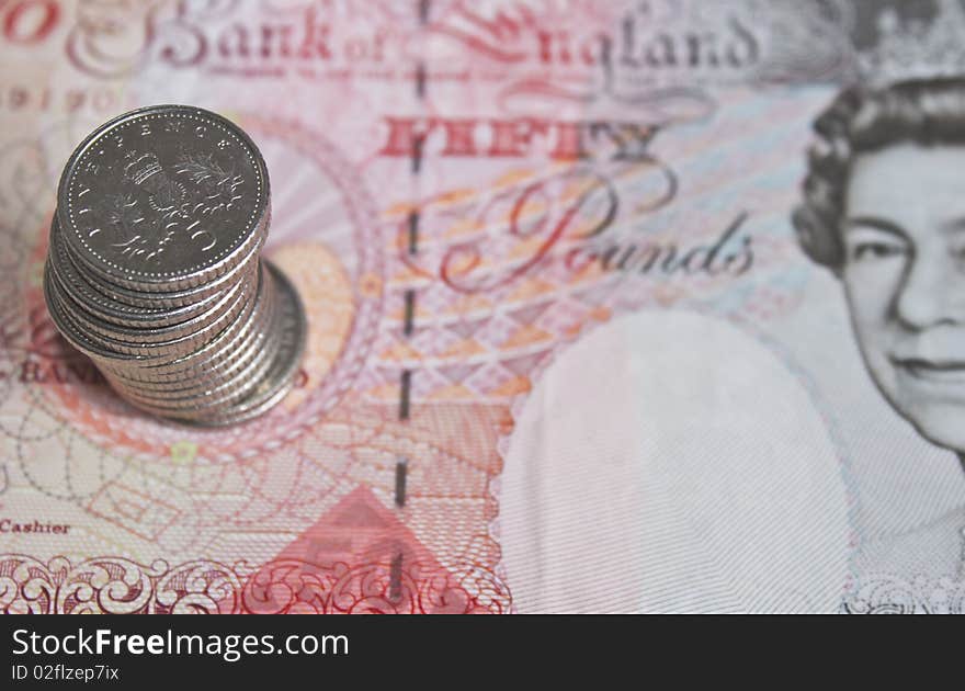 Some five pence pieces stacked on top of a fifty pound note in soft focus. Some five pence pieces stacked on top of a fifty pound note in soft focus