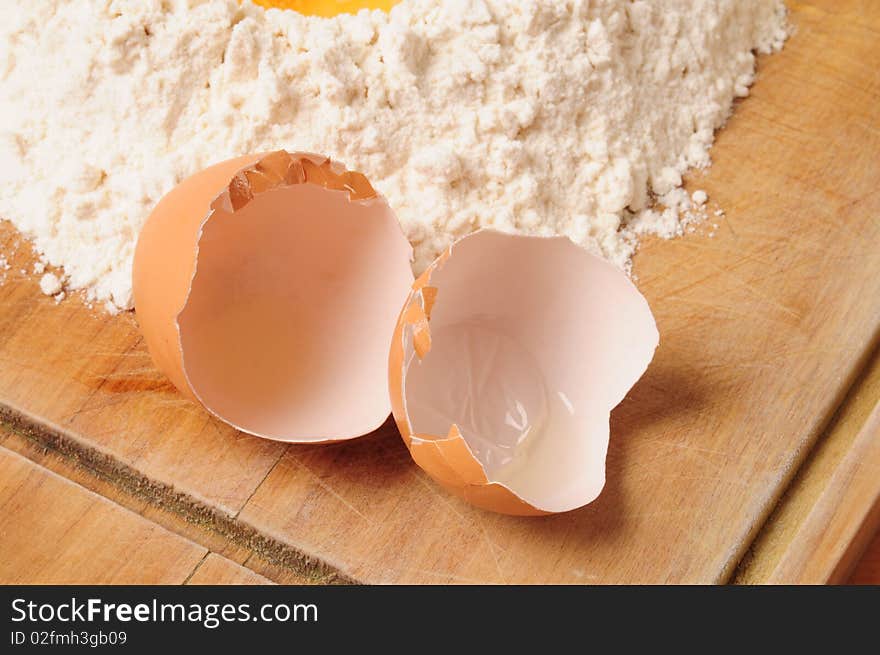 Empty egg next to white flour on cutting board. Empty egg next to white flour on cutting board.