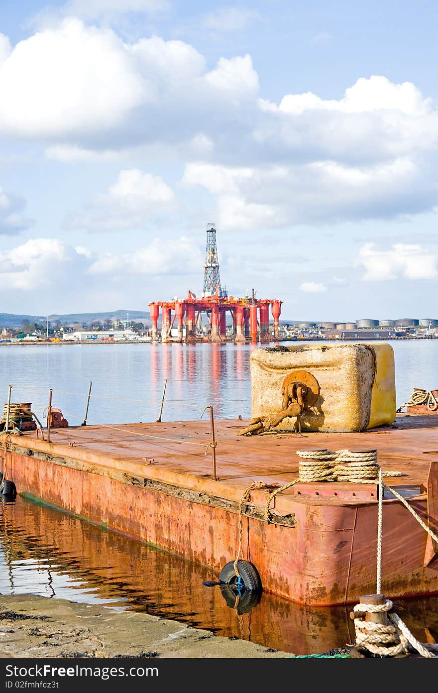 An image of a floating platform with an anchor weight on it and in the distance Invergordon with a large oil rig anchored in the port. An image of a floating platform with an anchor weight on it and in the distance Invergordon with a large oil rig anchored in the port.