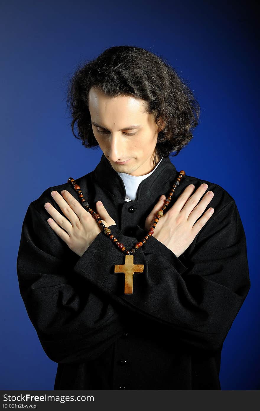 Conceptual portrait of Praying priest with wooden cross. blue background