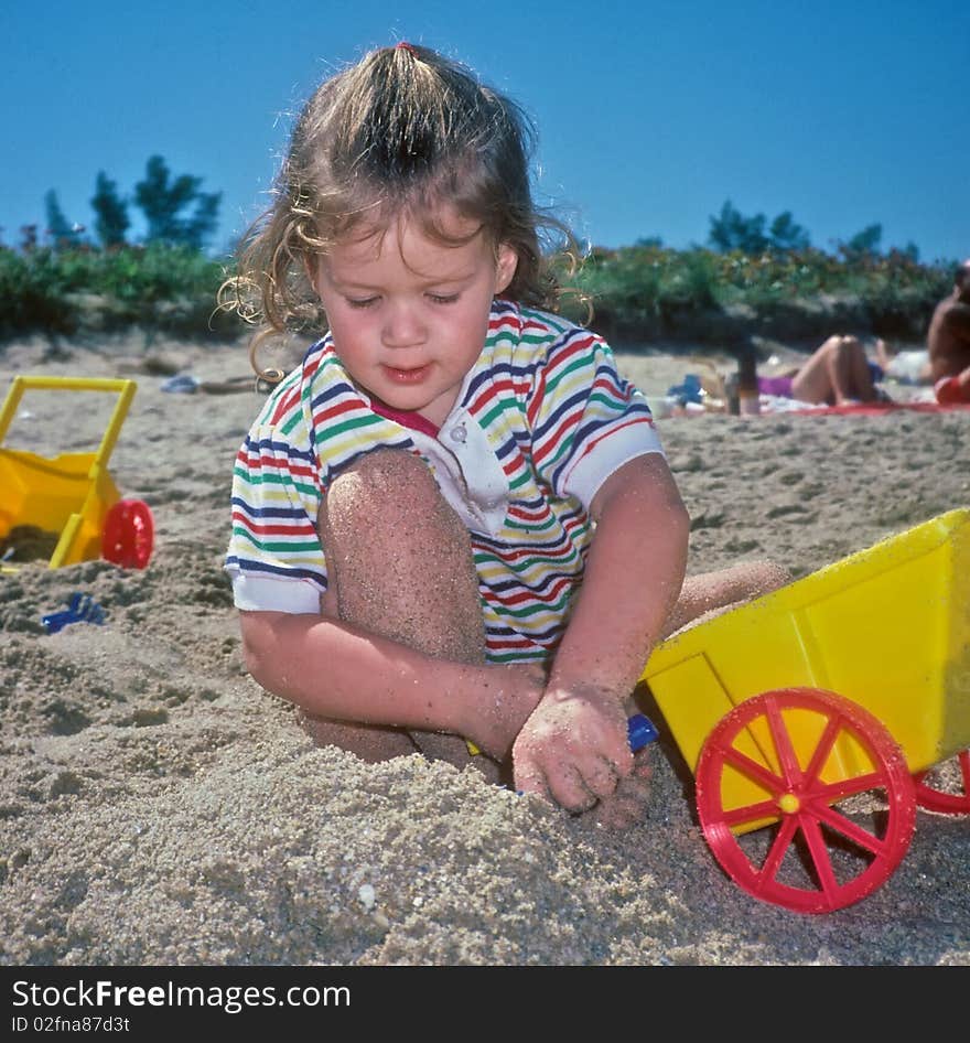 Little girl playing in sand on beach surrounded by beach toys. Little girl playing in sand on beach surrounded by beach toys