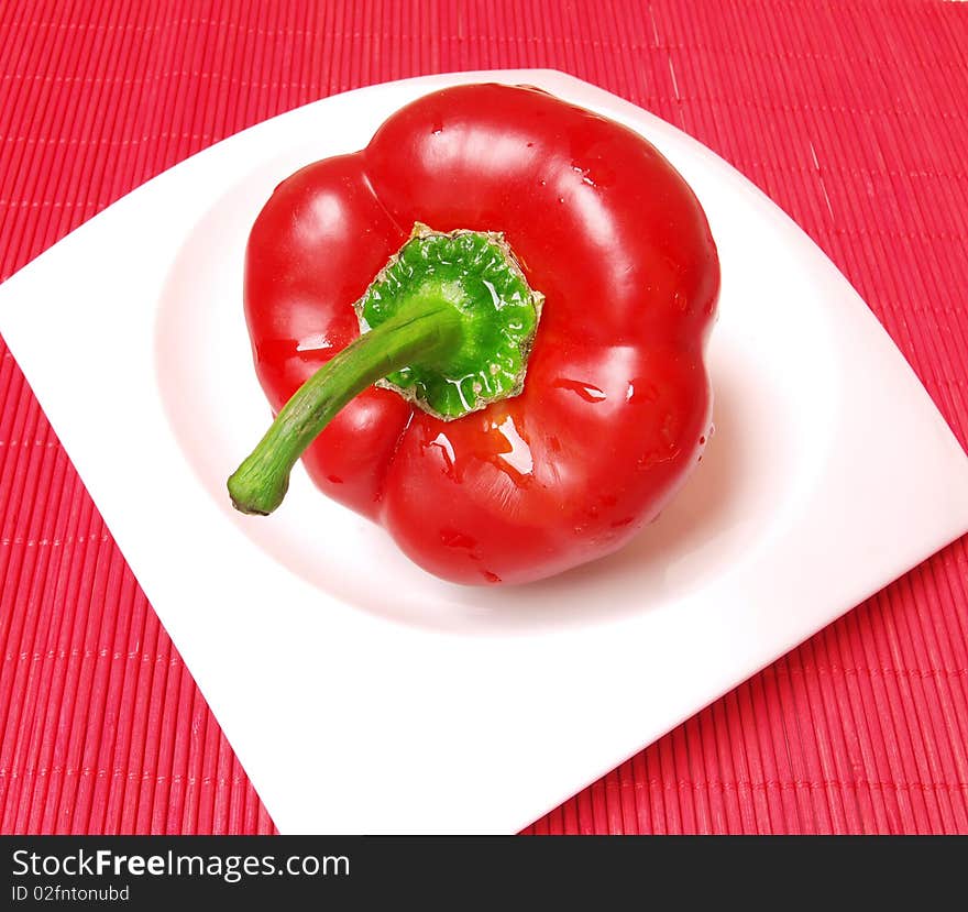 Red,wet,fresh pepper isolated on white plate on red background. Red,wet,fresh pepper isolated on white plate on red background