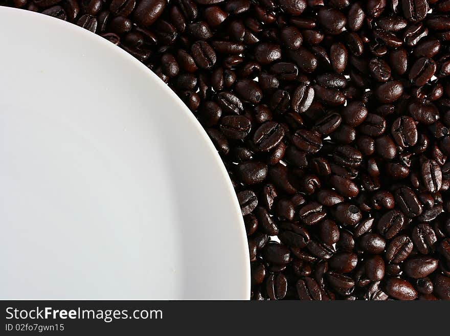 Coffee grains on a back background, from above there is a white plate.