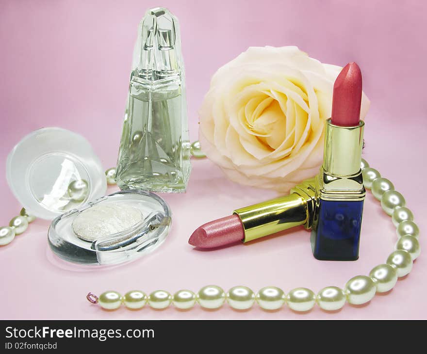 Red lipsticks yellow rose white eye-shadow and perfume on pink background. Red lipsticks yellow rose white eye-shadow and perfume on pink background