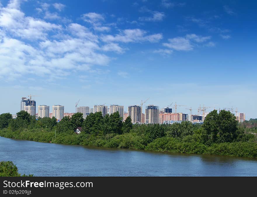 View of a some new residential buildings on a background of cloudy blue sky and river with green coast