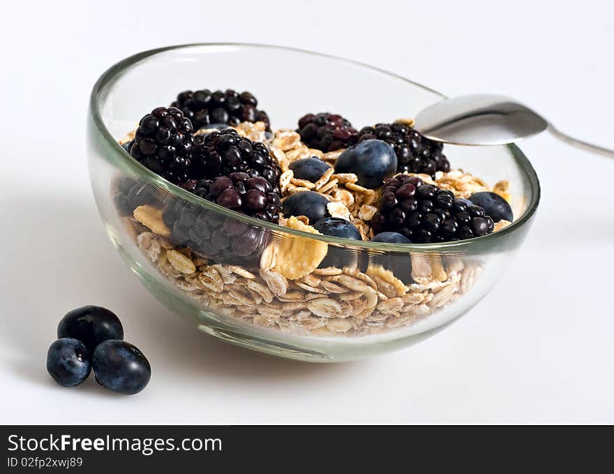 A glass bowl full of muesli, corn flakes, blackberries and blueberries. Selective focus. White background. A glass bowl full of muesli, corn flakes, blackberries and blueberries. Selective focus. White background.