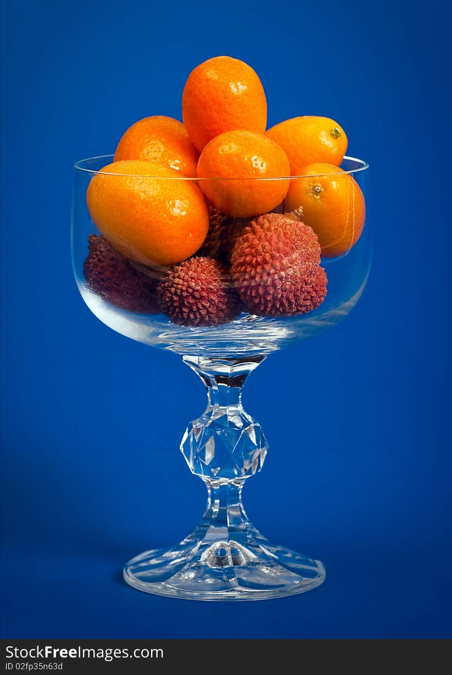 Kumquat and Litchi fruits in a crystal glass on a deep blue background