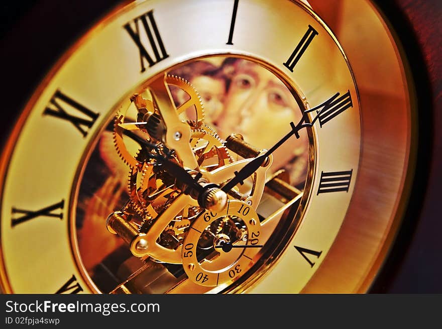 Open-gearing transparent clock with the Virgin Mary icon appearing through glass, blur background. Open-gearing transparent clock with the Virgin Mary icon appearing through glass, blur background