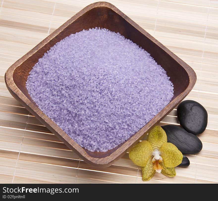 Spa scene with orchids, bath salts and massage stones on a bamboo mat.