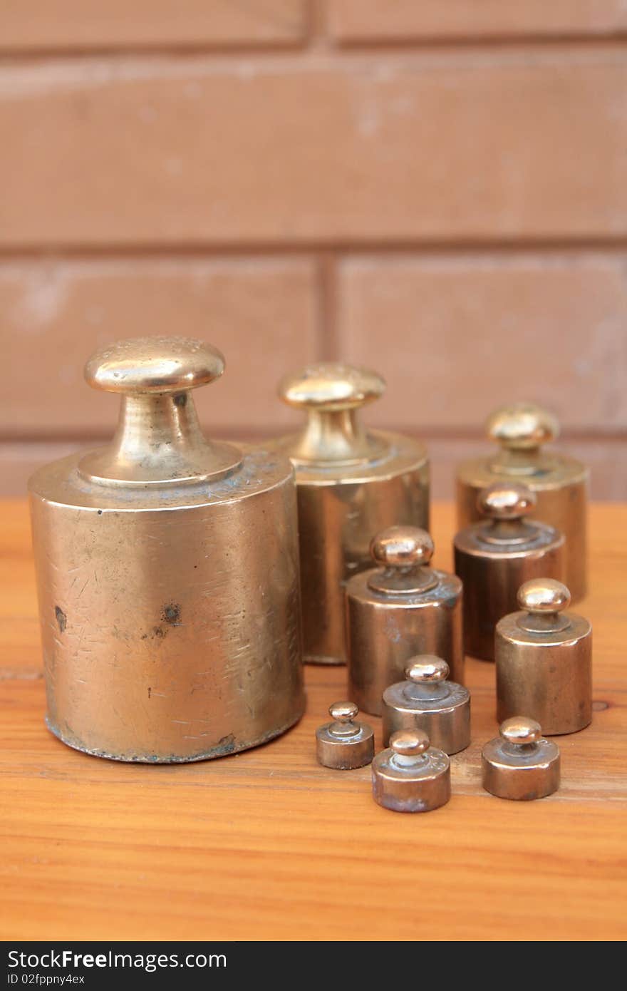 Antique weights from an old scale, made of brass, on a wooden surface and with a brick background. Antique weights from an old scale, made of brass, on a wooden surface and with a brick background