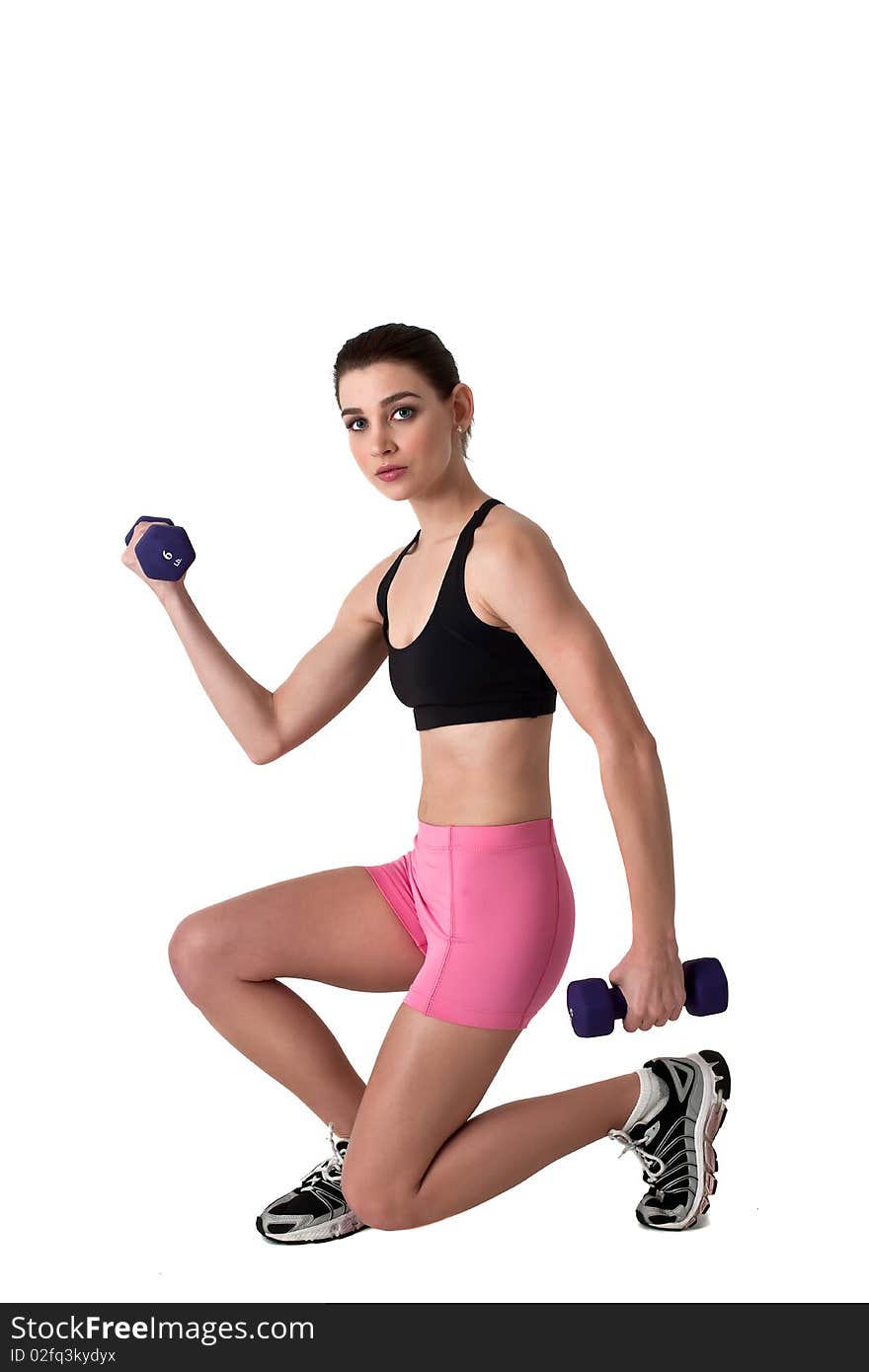 Beautiful young brunette woman with blue eyes exercising with dumbbells in black top and pink shorts. Beautiful young brunette woman with blue eyes exercising with dumbbells in black top and pink shorts