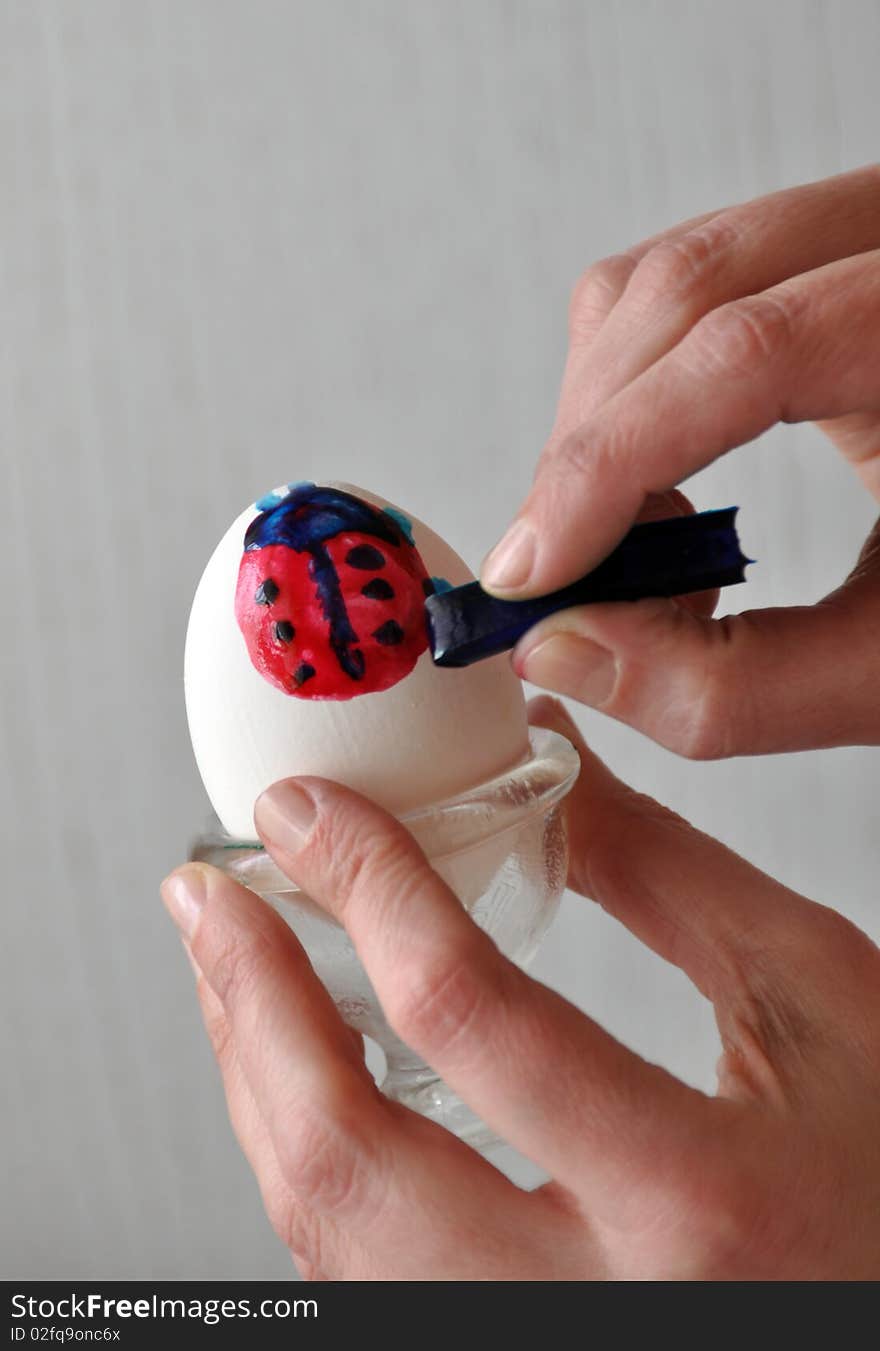 Female hands coloring an easter egg - painting a ladybug on it - behind gray. Female hands coloring an easter egg - painting a ladybug on it - behind gray