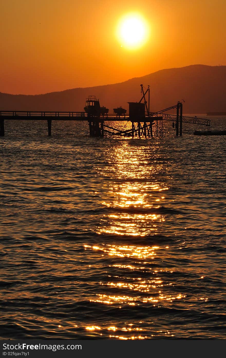 Warm sunset over the sea with silhouetted dock and mountain. Warm sunset over the sea with silhouetted dock and mountain.