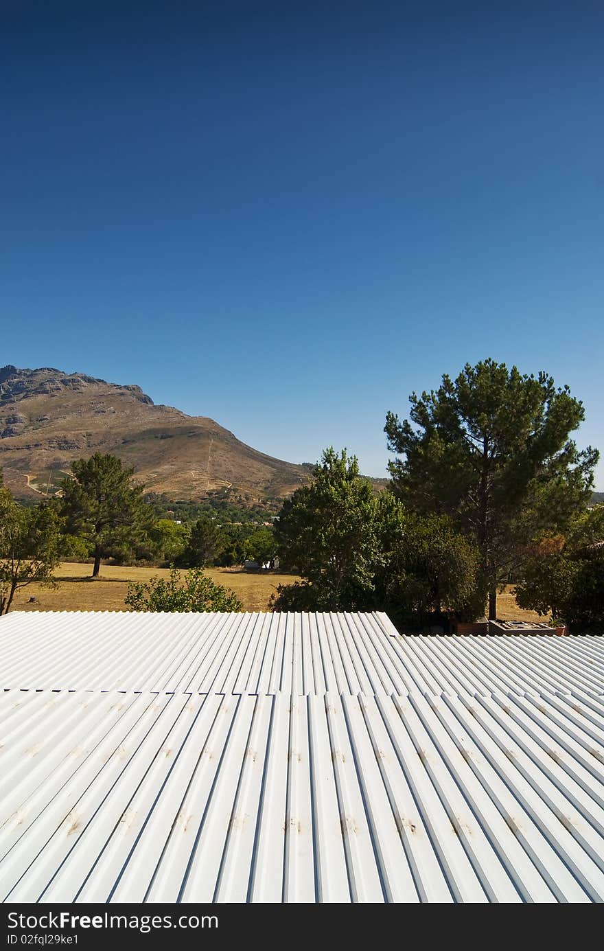 White sink roof of a modern hosue overlooking a mountain range with clear blue skies overhead. White sink roof of a modern hosue overlooking a mountain range with clear blue skies overhead