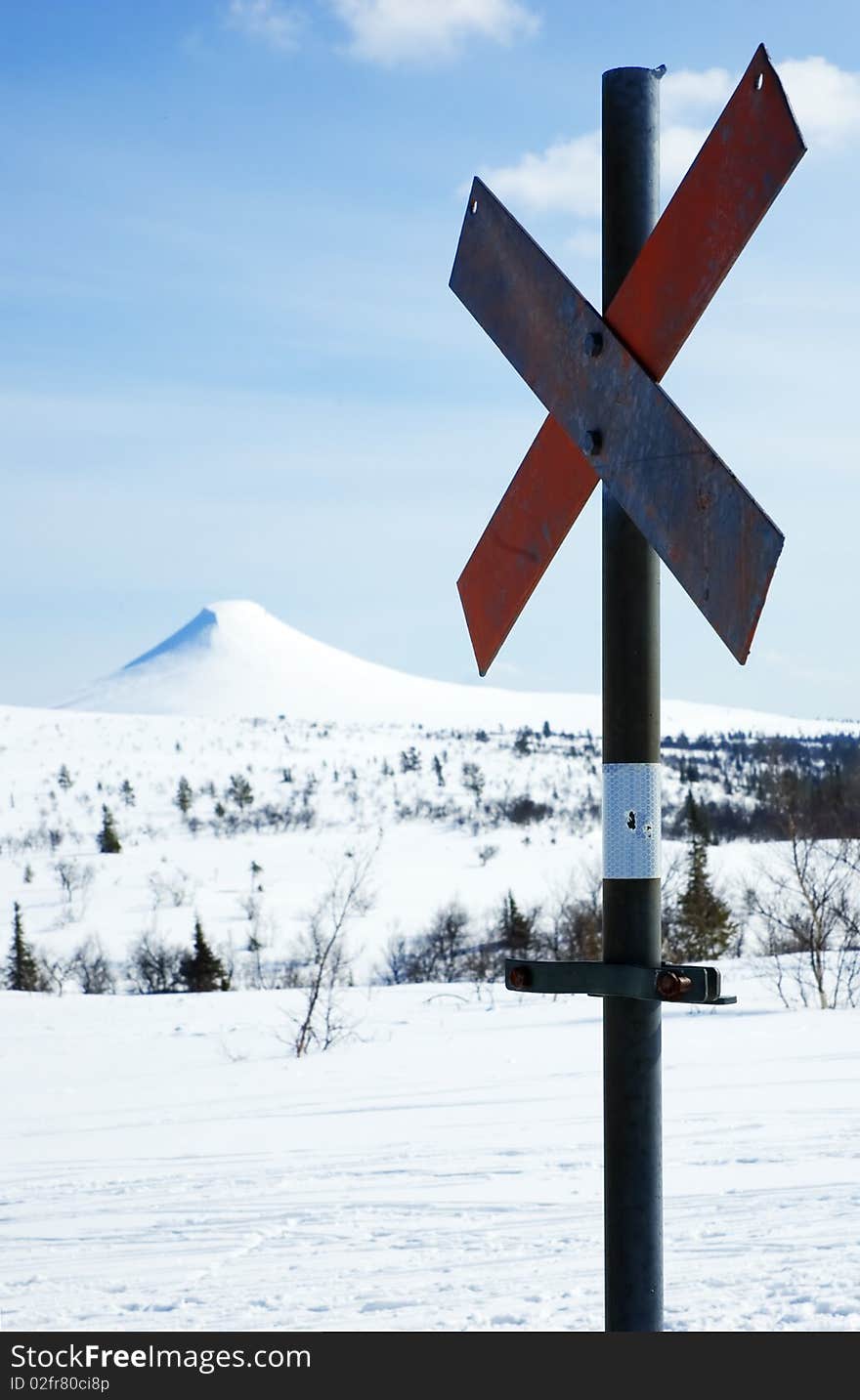 A rusty ski trail marker against a snow covered mountain.