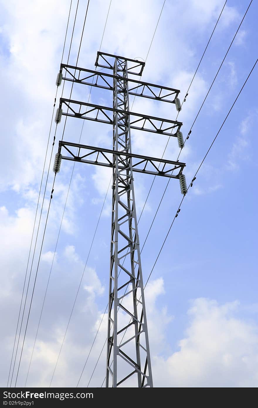 Support metal high-voltage with isolators and wires on a background of the blue sky with clouds.