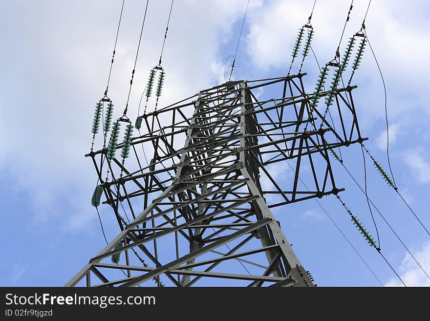 Support metal high-voltage with isolators and wires on a background of the blue sky with clouds.