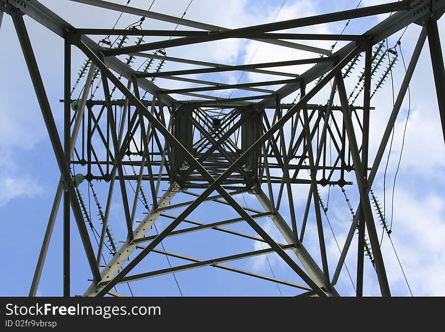 Support metal high-voltage with isolators and wires on a background of the blue sky with clouds.