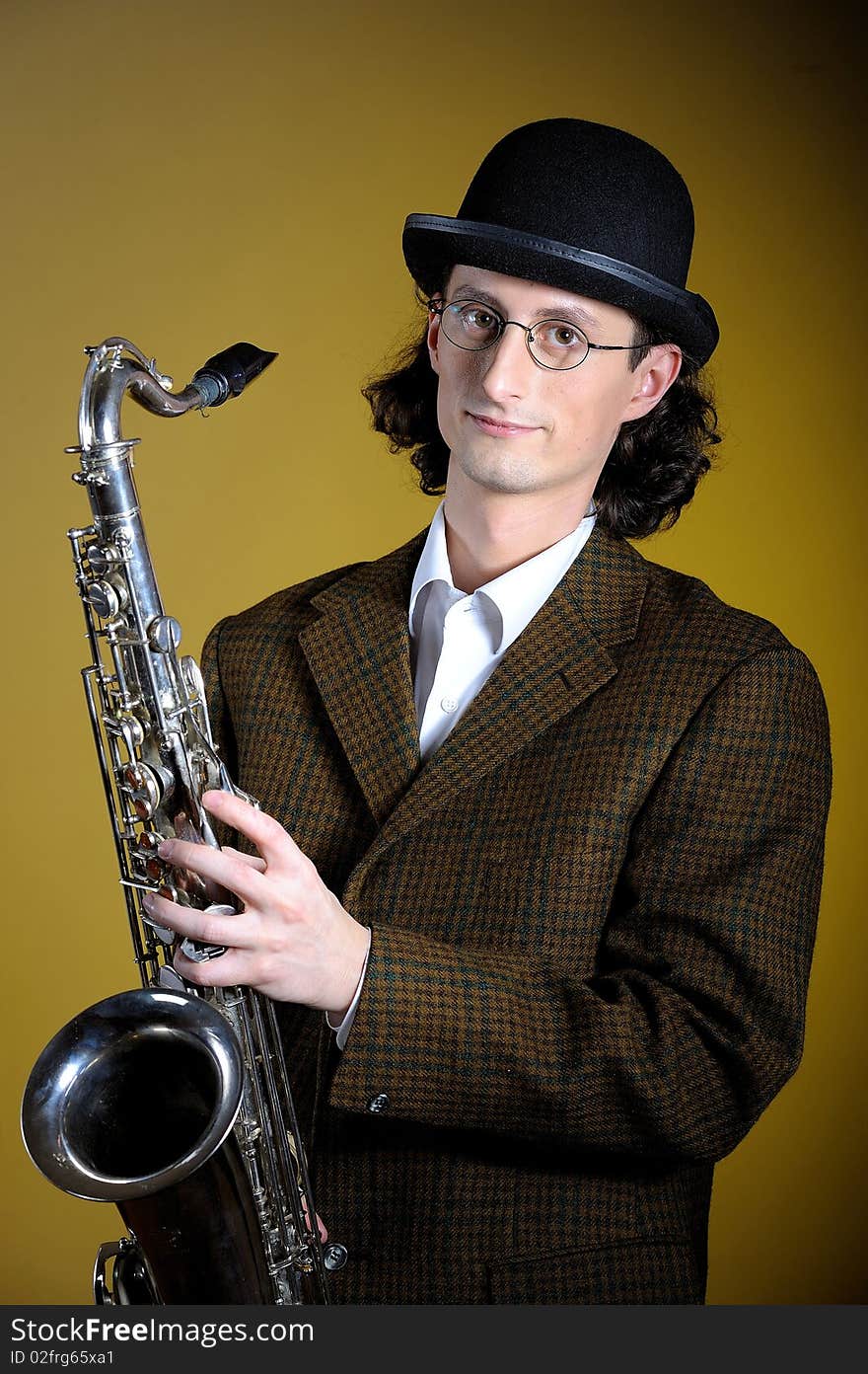 Portrait of young english gentleman in bowler hat holding saxophone. yellow background