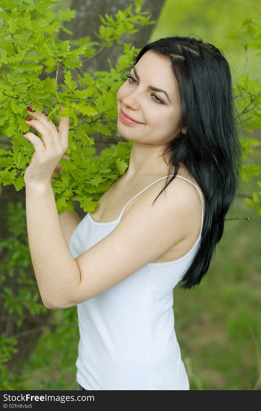 Young woman in forest touches oak leaves.